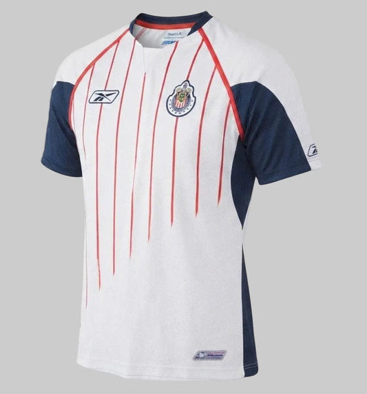 Vista frontal detallada del jersey de visitante Reebok de las Chivas de Guadalajara 2005/06 (código AMML5004) sobre fondo blanco, mostrando el escudo bordado del club y el logotipo de Reebok, disponible en Futbol90MX