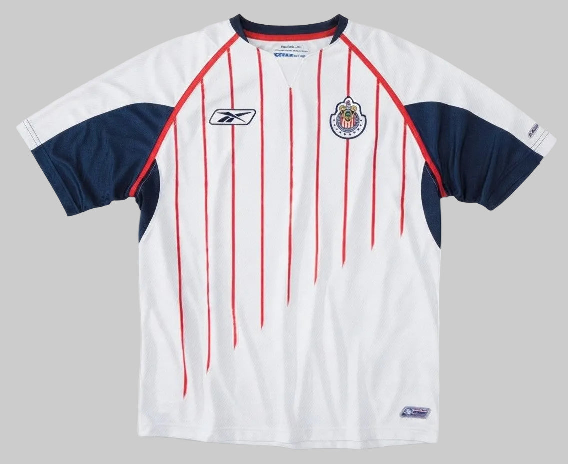 Vista de detalle del cuello en V y el hombro del jersey de visita de Chivas 2005/06, resaltando los ribetes en azul marino y rojo.